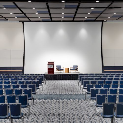 A large conference or lecture hall with a stage, a projector screen, and an empty audience seated in rows. Top it at 140 characters, always ending the sentence.