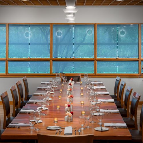 A long conference or classroom with rows of chairs facing a stage or lectern, blue walls, and a high ceiling; people seated or standing near the front.